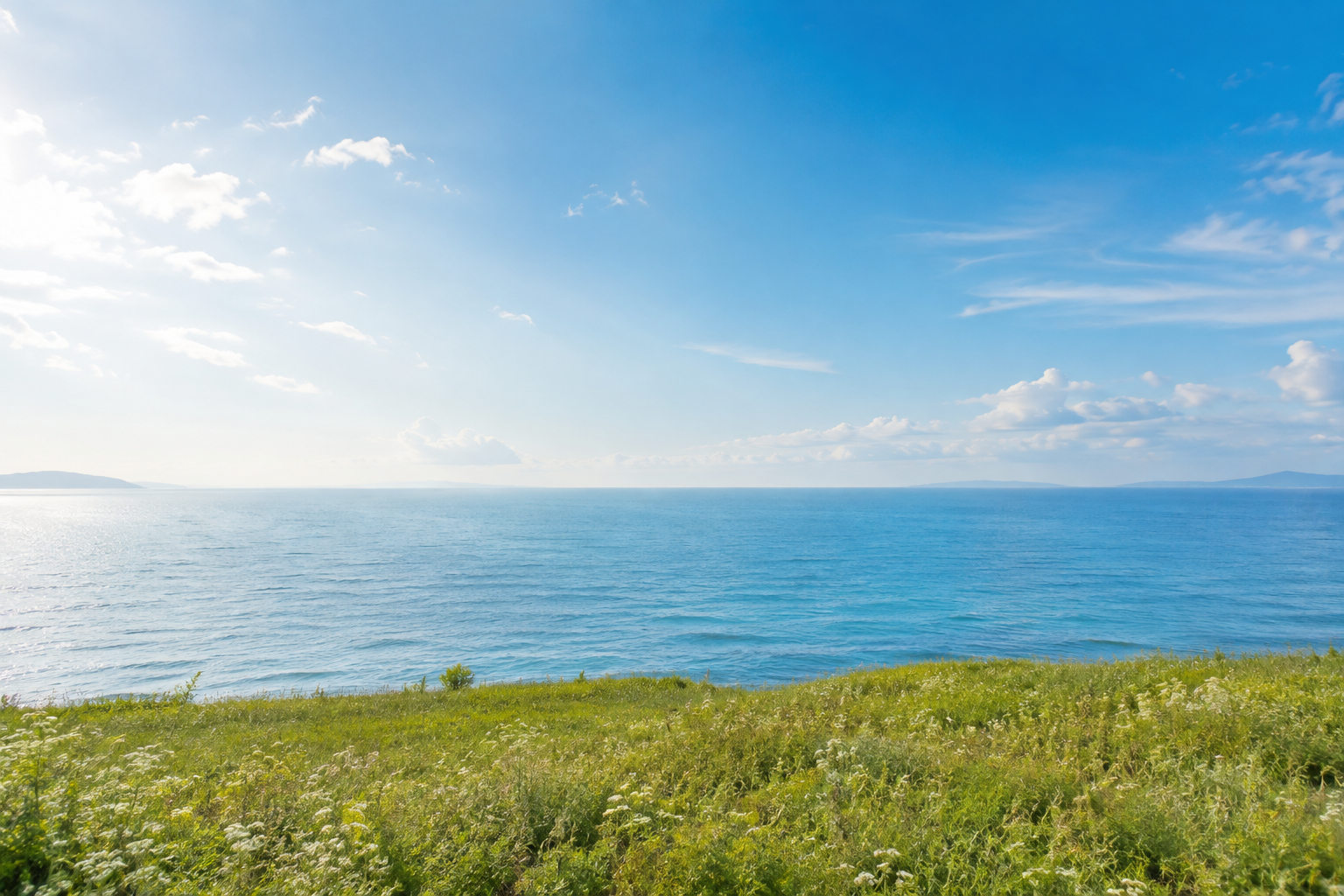 青い空と穏やかな海、緑の草原が広がる開放的な自然風景
